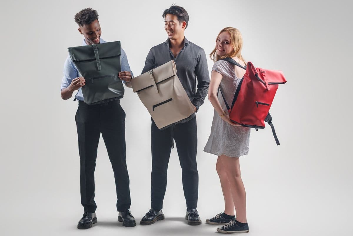 Three models holding NORJ backpacks in green, white, and red