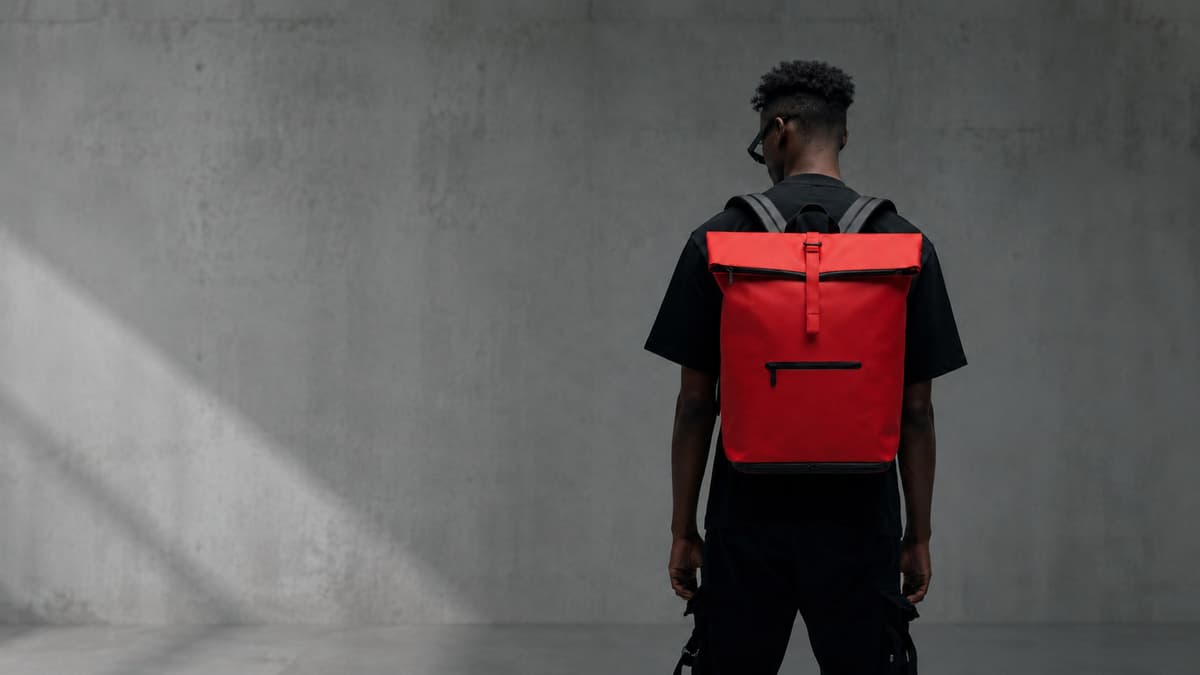 Model wearing NORJ red backpack against concrete wall